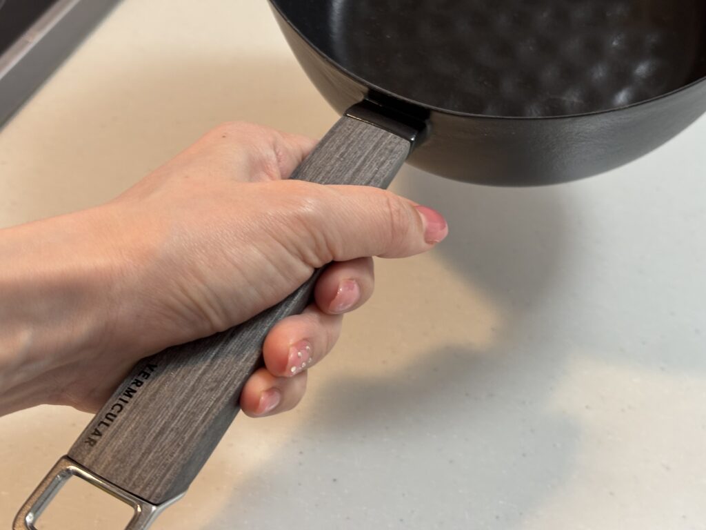 VERMICULARユキヒラ鍋18cmを手にした使用イメージ。木製ハンドルが手にフィットしやすいデザイン
