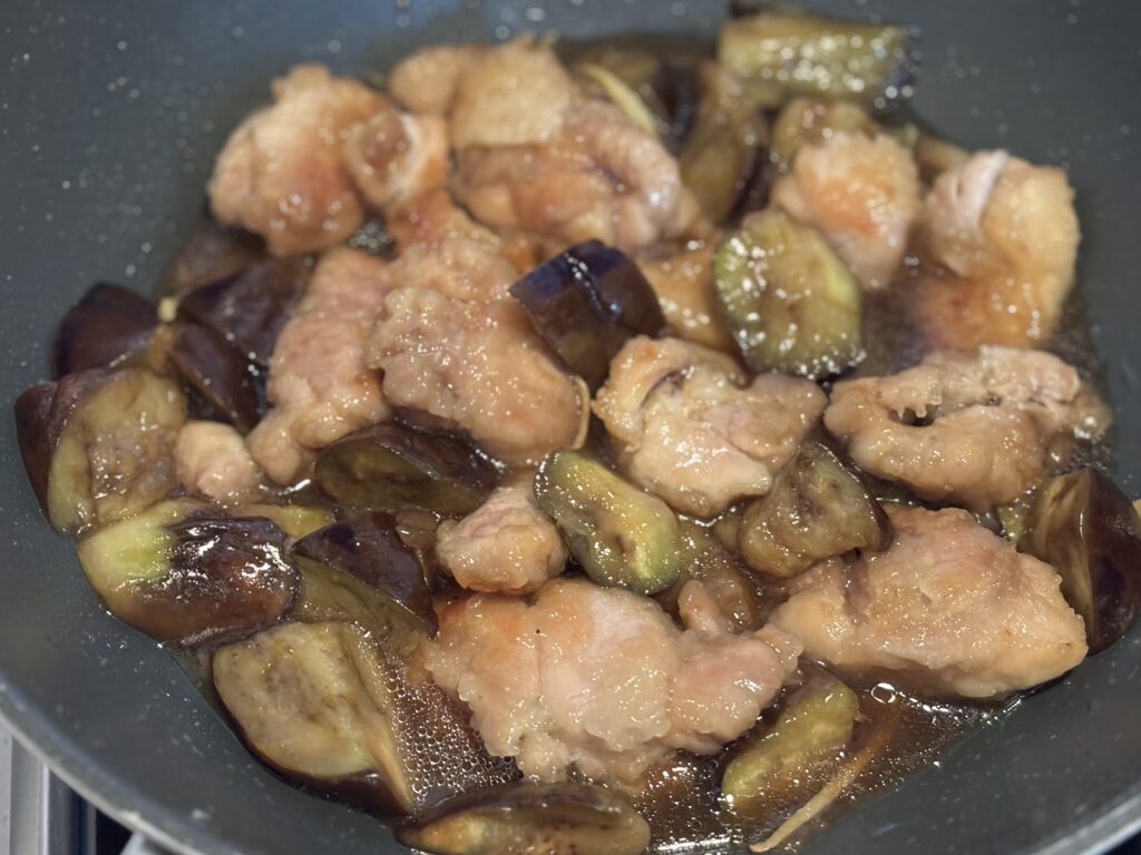炒めた鶏肉とナスに調味料を加えて煮絡めている様子。全体がとろりとしたタレで艶やかに。