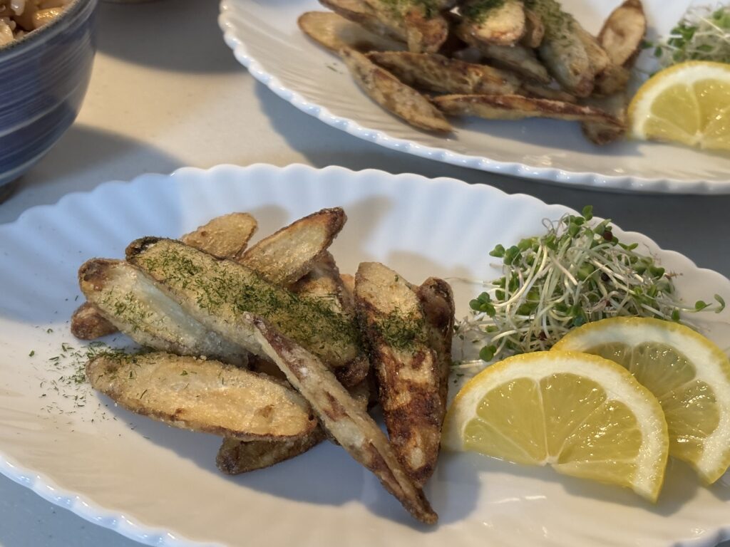 ごぼうの唐揚げとスプラウト、レモンを盛り付けた白い皿。食卓の副菜としての和風メニュー。