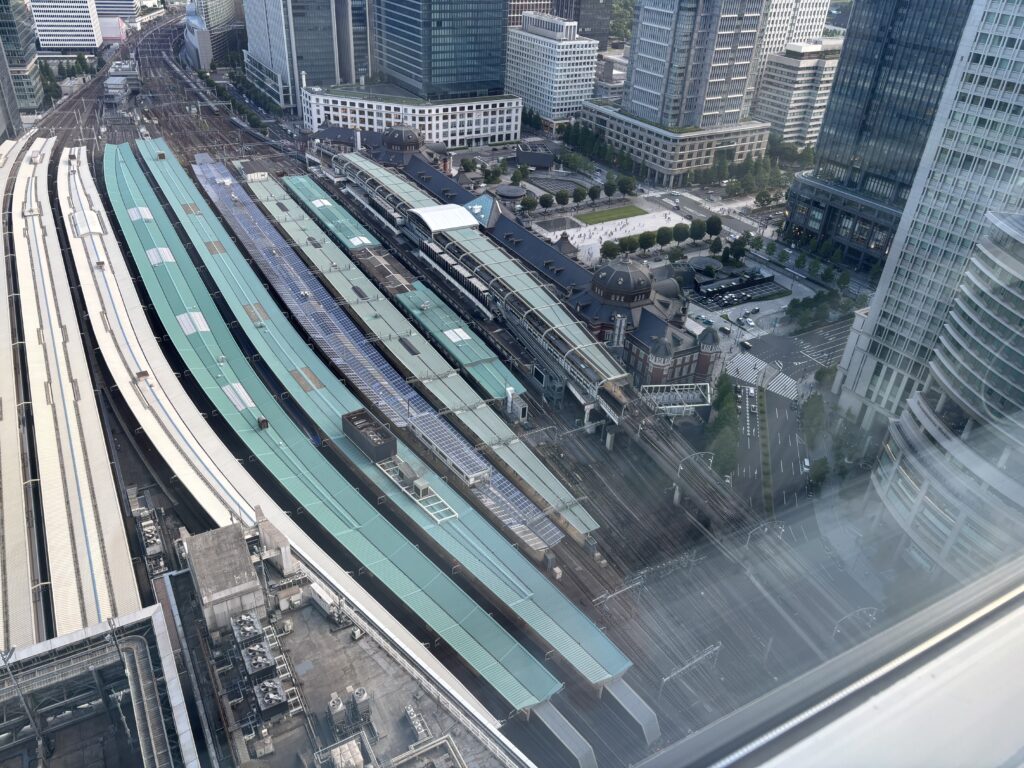 窓から見下ろす東京駅全景「高層階から見下ろした東京駅丸の内駅舎とホーム。周囲のオフィス街や行き交う列車が一望できる景色。」
