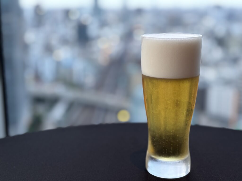 ビール「東京の街並みを背景に、きめ細かな泡がのった生ビールのグラス。」