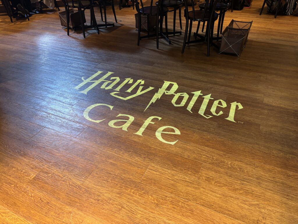 ハリーポッターカフェの店内、木目調の床にライトで投影されたHarry Potter Cafeのロゴ